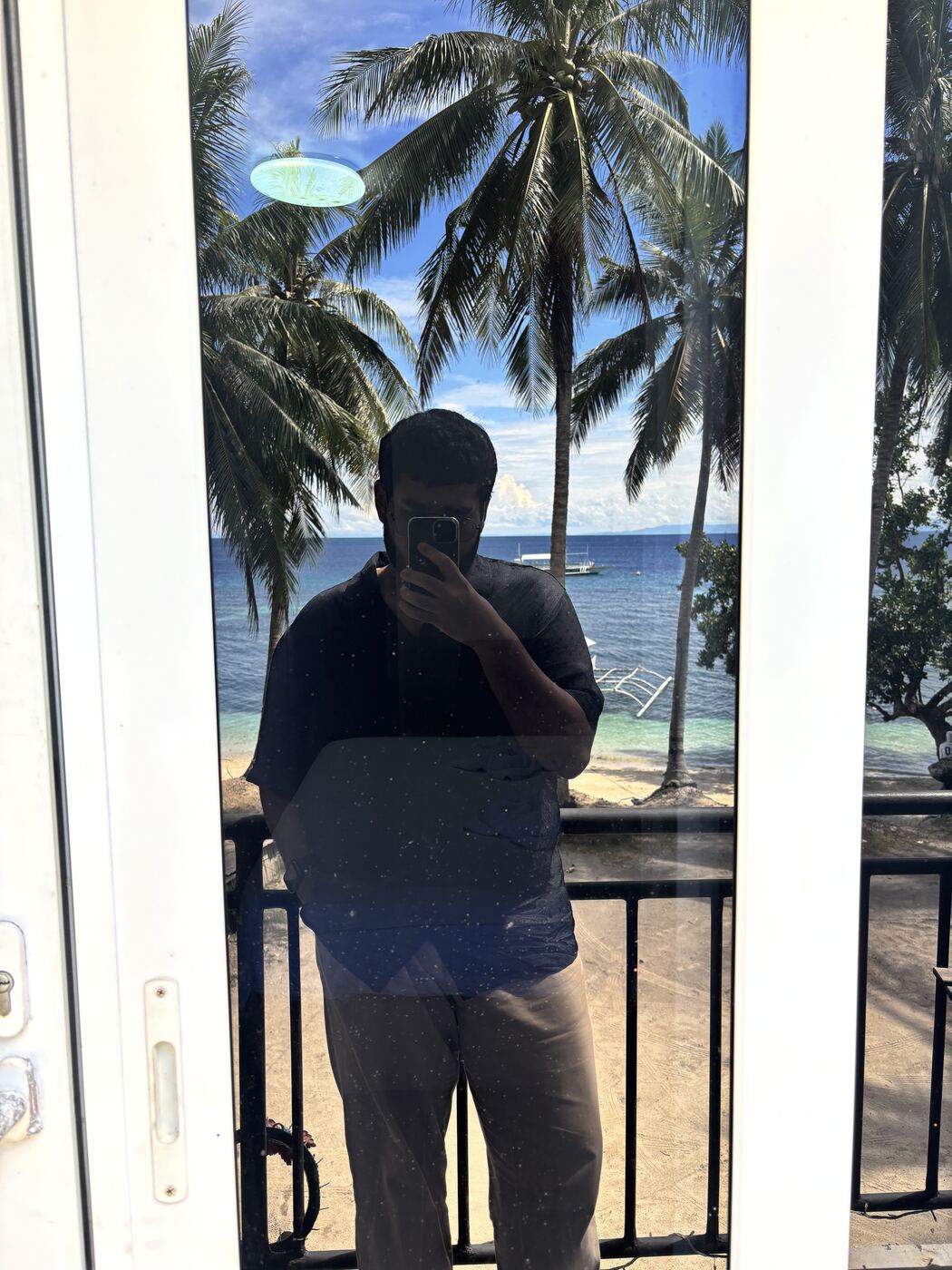 Mirror selfie on a balcony overlooking palm trees and the sea